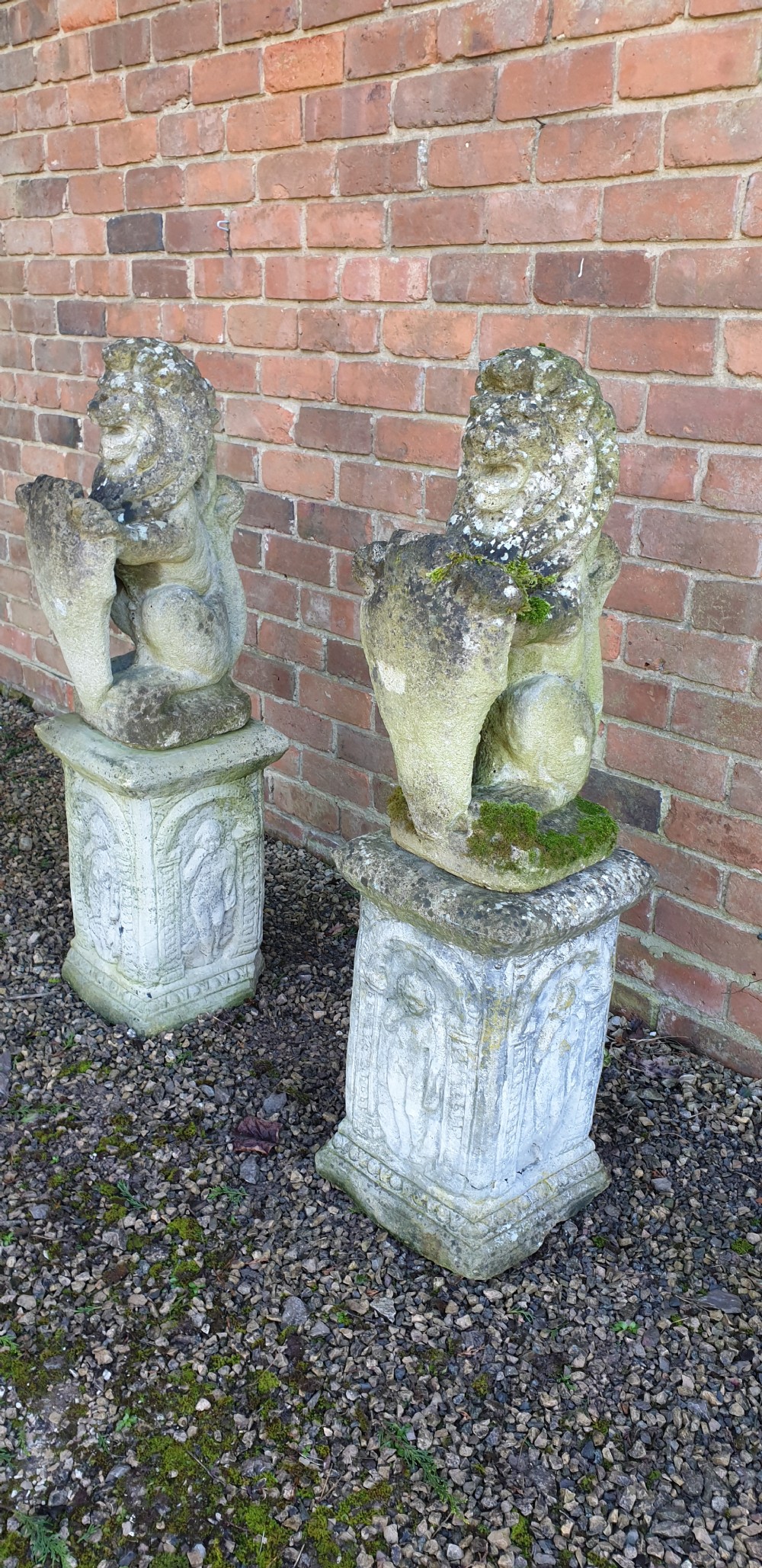 A pair of weathered grey stone seated lion statues holding shields, mounted on relief-carved rectangular plinths. View V