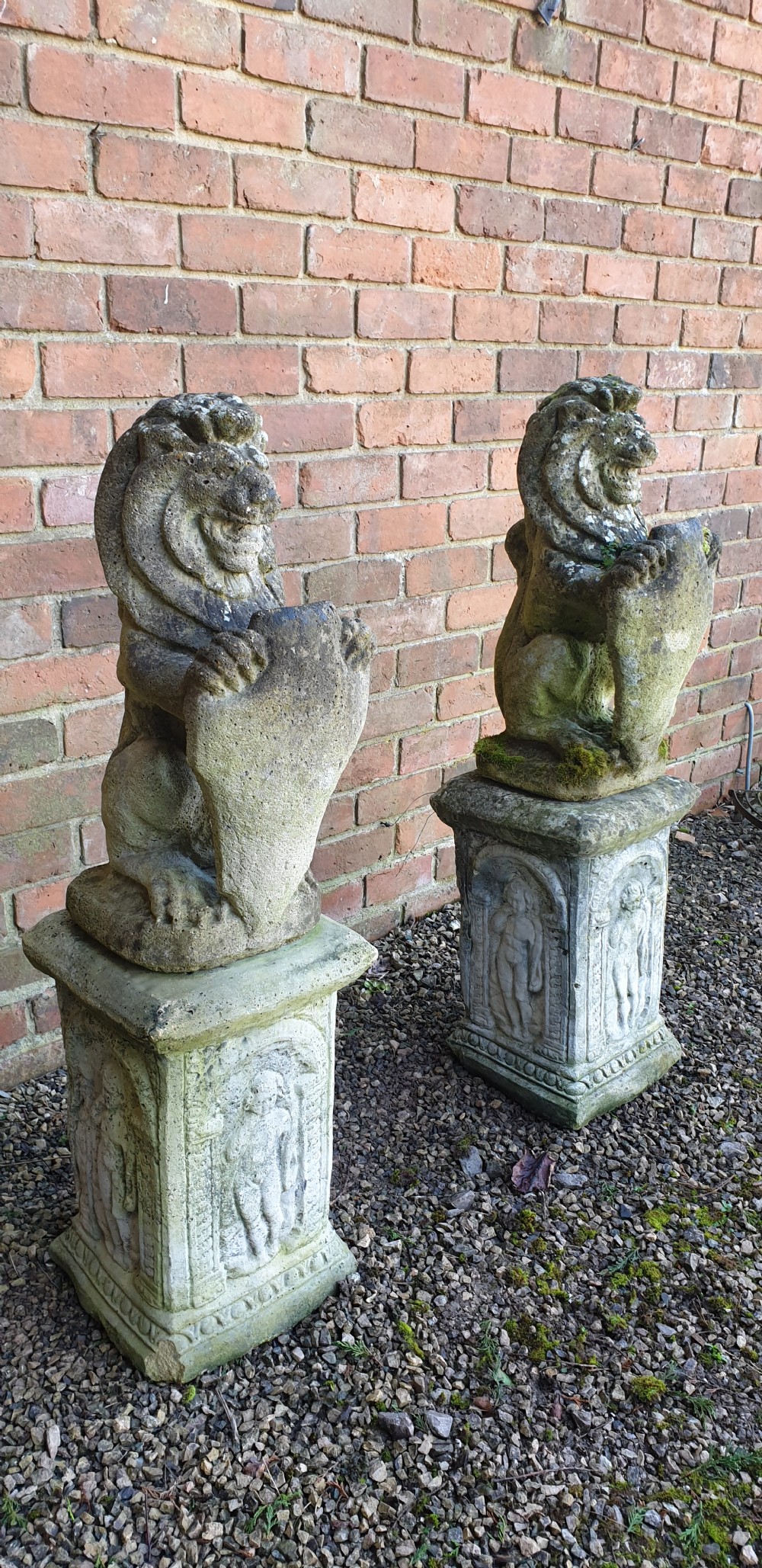 A pair of weathered grey stone seated lion statues holding shields, mounted on relief-carved rectangular plinths. View VII