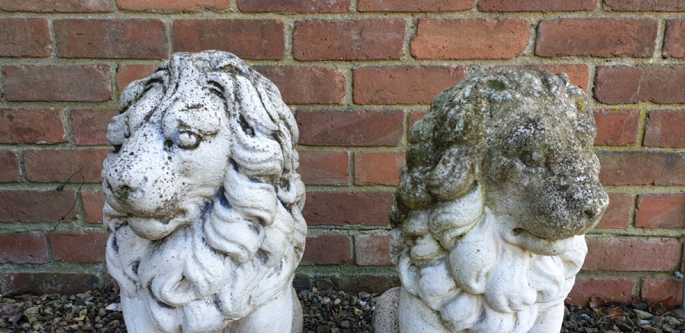 A pair of weathered off-white reconstituted stone lion statues rendered in a seated pose atop integral rectangular bases. View II