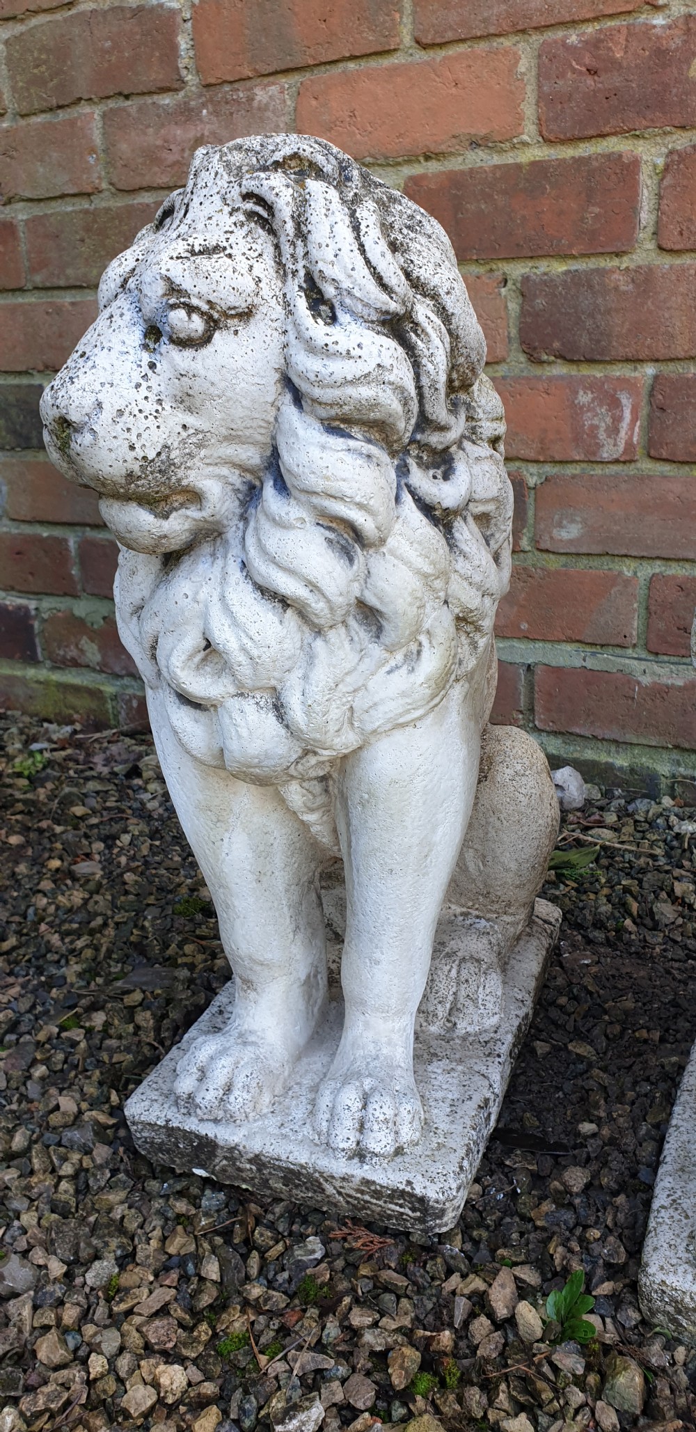 A pair of weathered off-white reconstituted stone lion statues rendered in a seated pose atop integral rectangular bases. View III