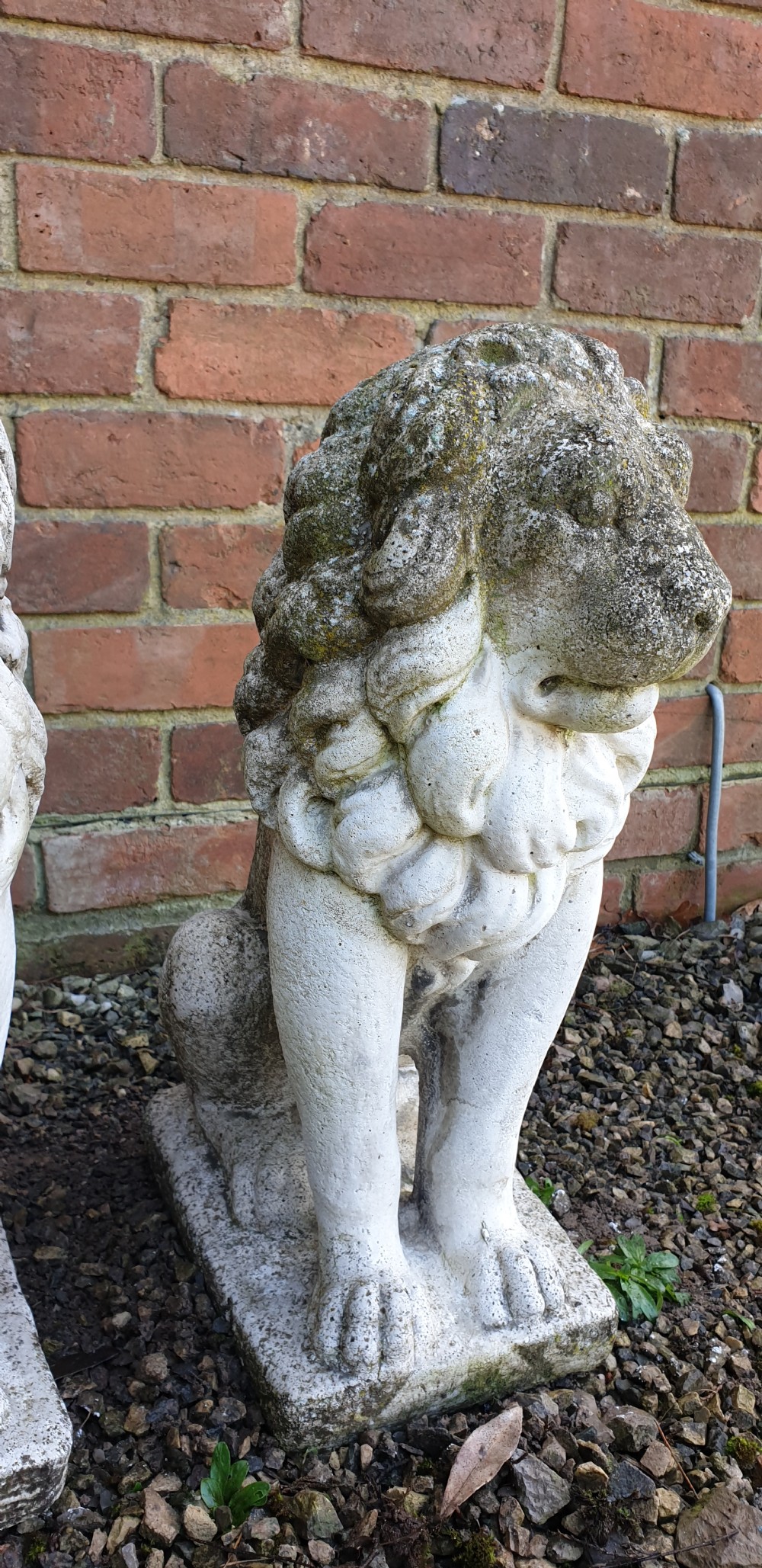 A pair of weathered off-white reconstituted stone lion statues rendered in a seated pose atop integral rectangular bases. View IV