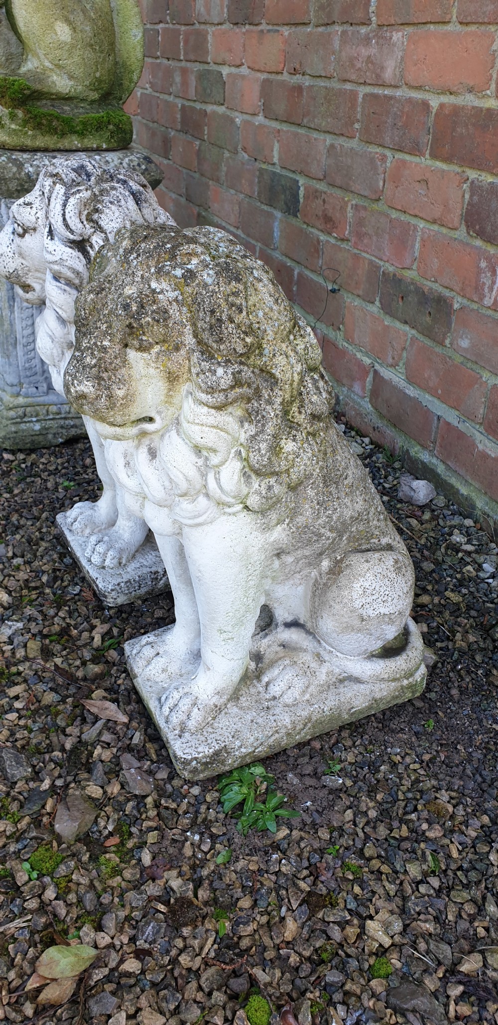A pair of weathered off-white reconstituted stone lion statues rendered in a seated pose atop integral rectangular bases. View V