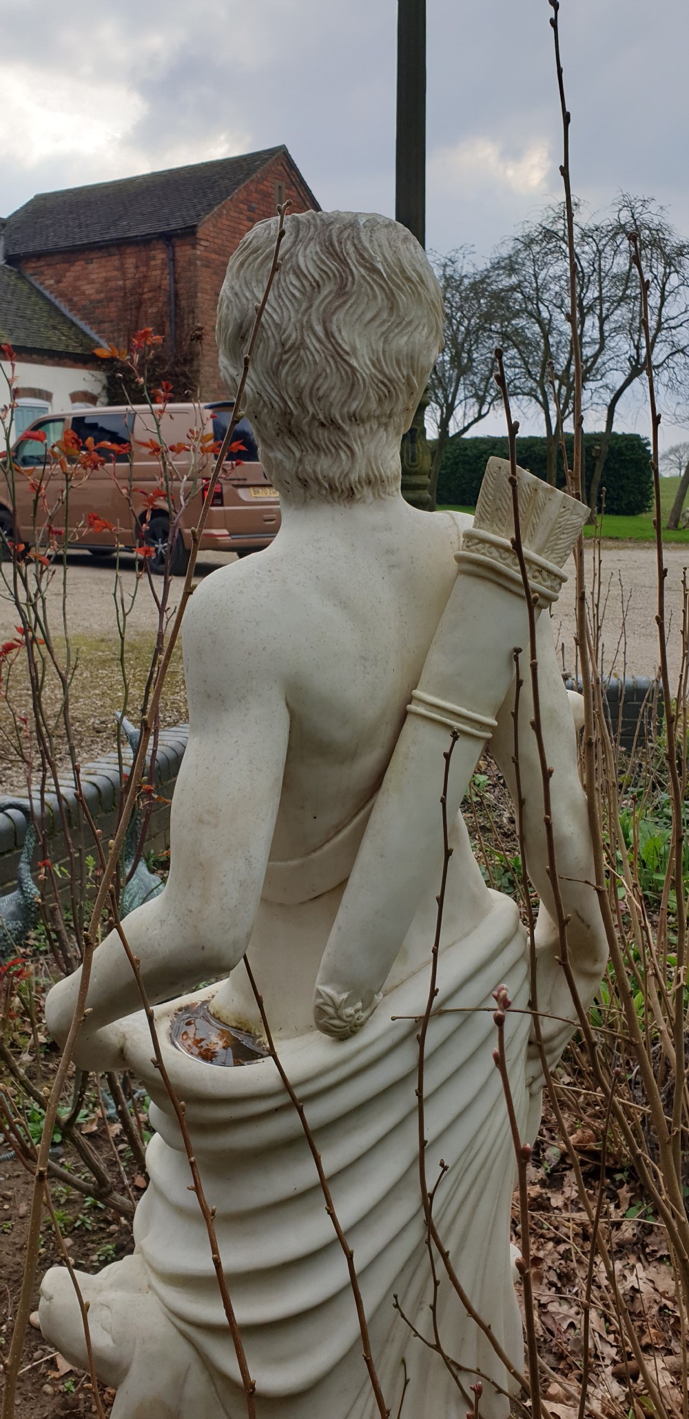 A life-sized off-white stone statue depicting a draped classical male figure holding a bow with a quiver on his back, set on a square plinth. View IV