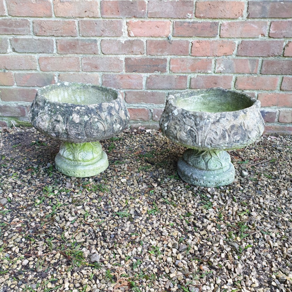 A matching pair of heavy round stone garden planters with carved leaf motifs and natural moss weathering.