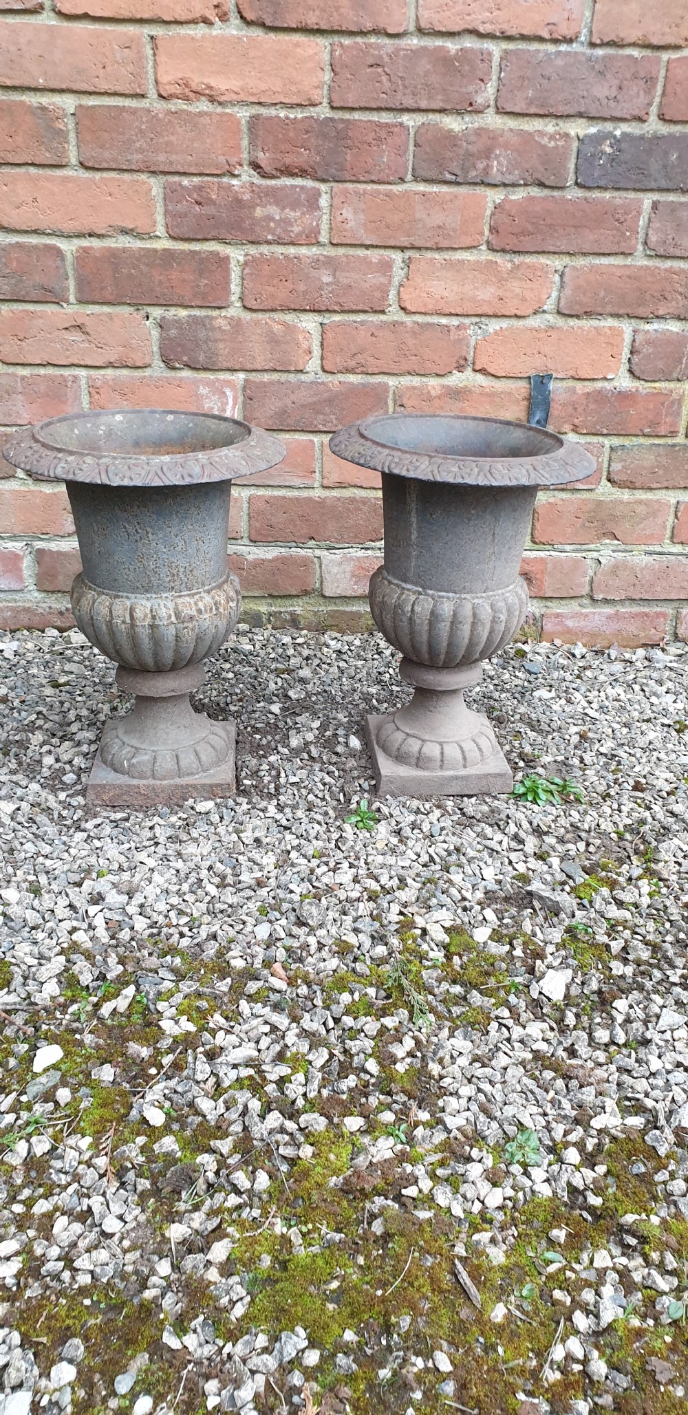 A pair of classical cast iron garden urns featuring gadrooned bodies, decorative flared rims, and square bases with a weathered patina.