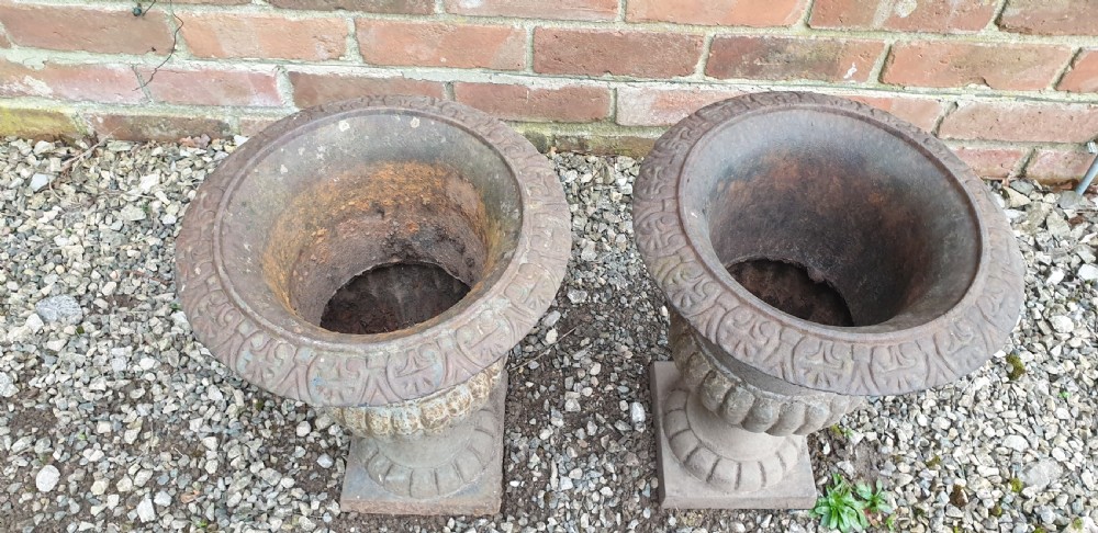 A pair of classical cast iron garden urns featuring gadrooned bodies, decorative flared rims, and square bases with a weathered patina. View II