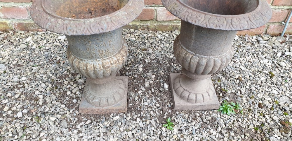 A pair of classical cast iron garden urns featuring gadrooned bodies, decorative flared rims, and square bases with a weathered patina. View III