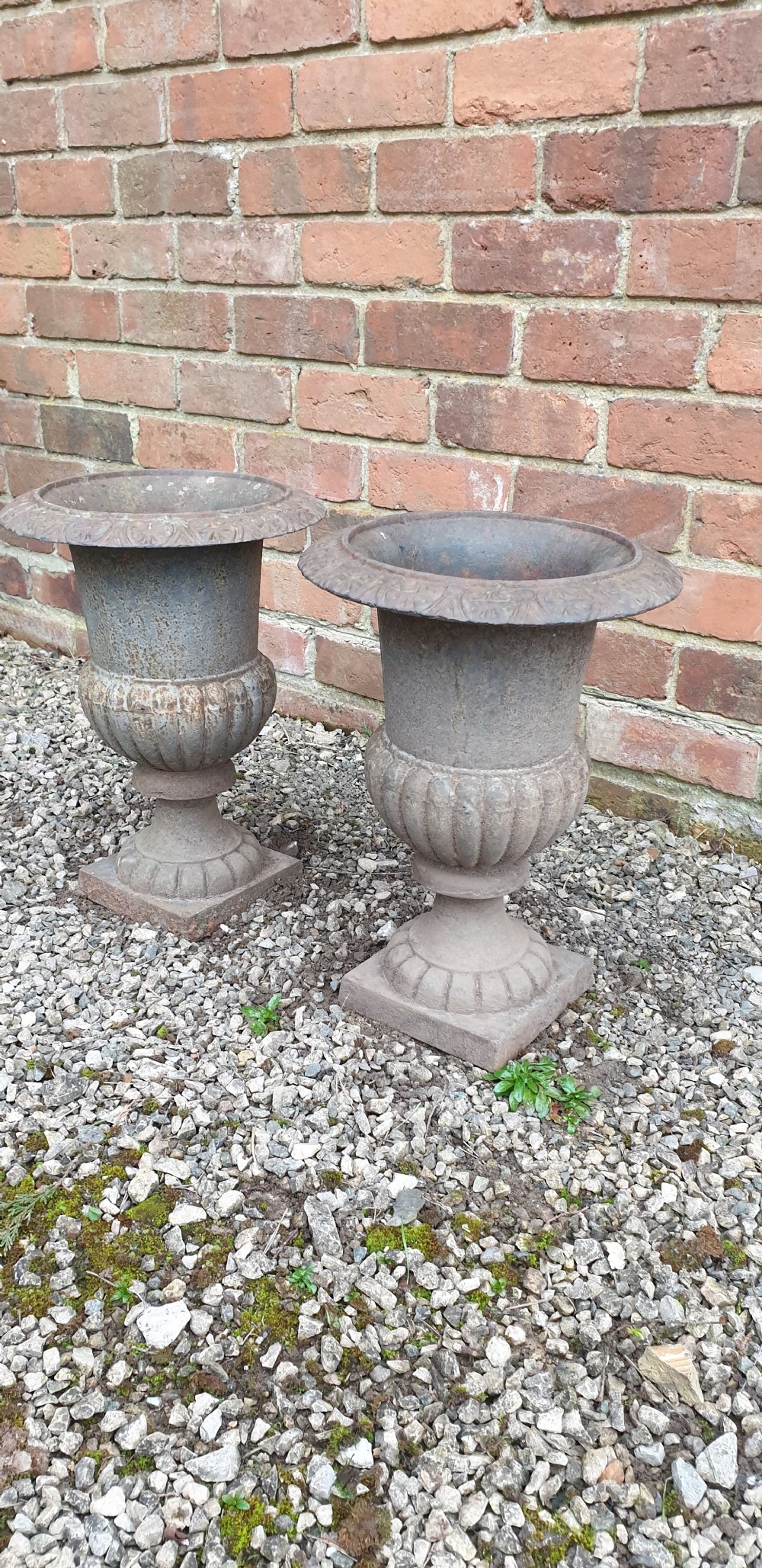 A pair of classical cast iron garden urns featuring gadrooned bodies, decorative flared rims, and square bases with a weathered patina. View V