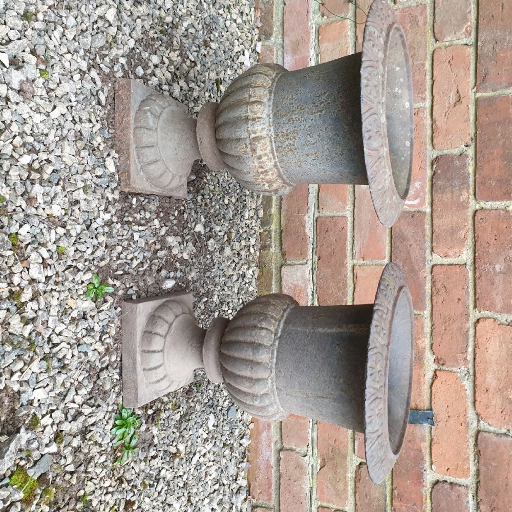 A pair of classical cast iron garden urns featuring gadrooned bodies, decorative flared rims, and square bases with a weathered patina. View VI
