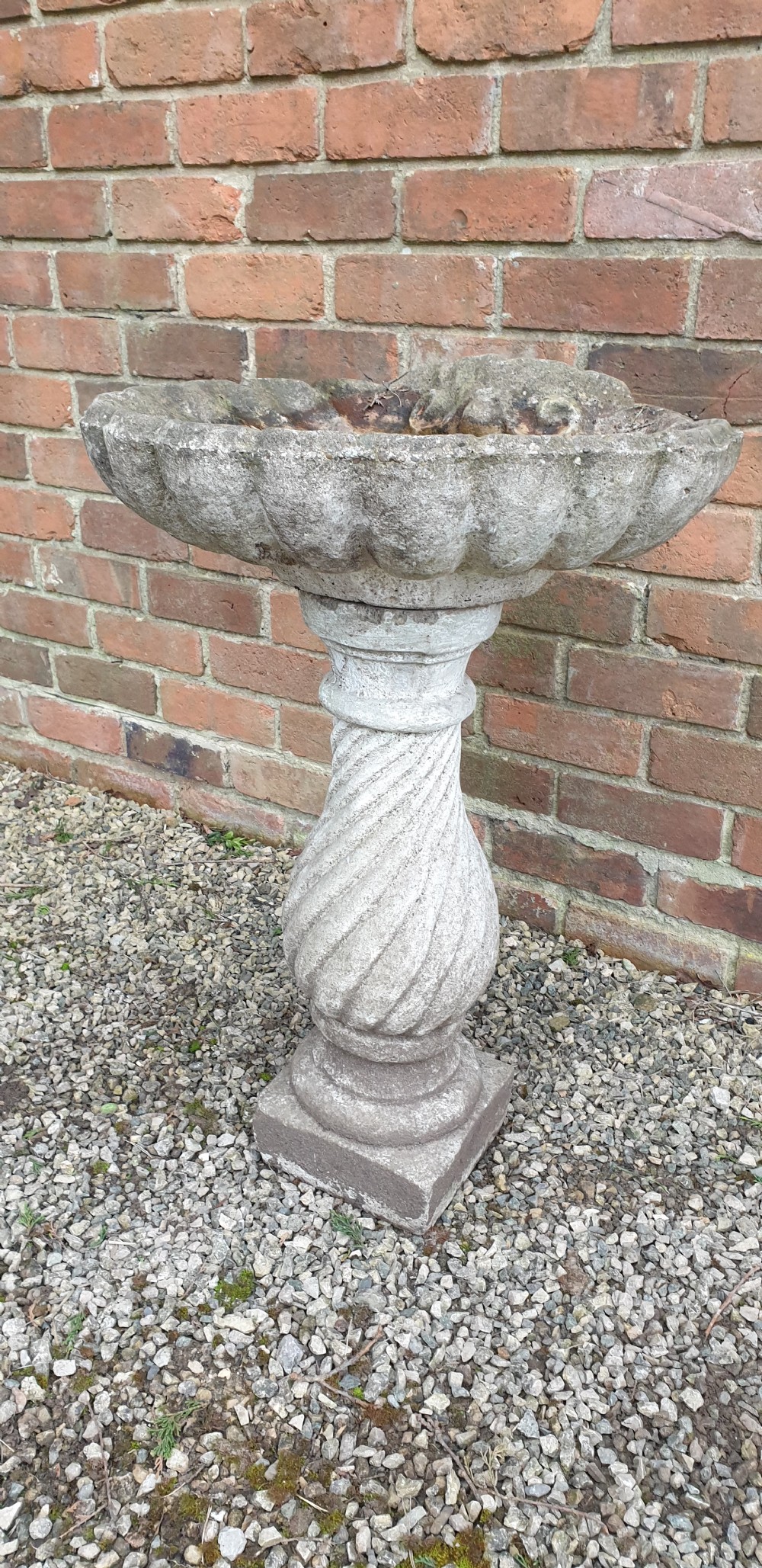 A weathered grey stone bird bath featuring a scalloped shell-shaped top basin set upon a spiral twisted pedestal column and square base. View II