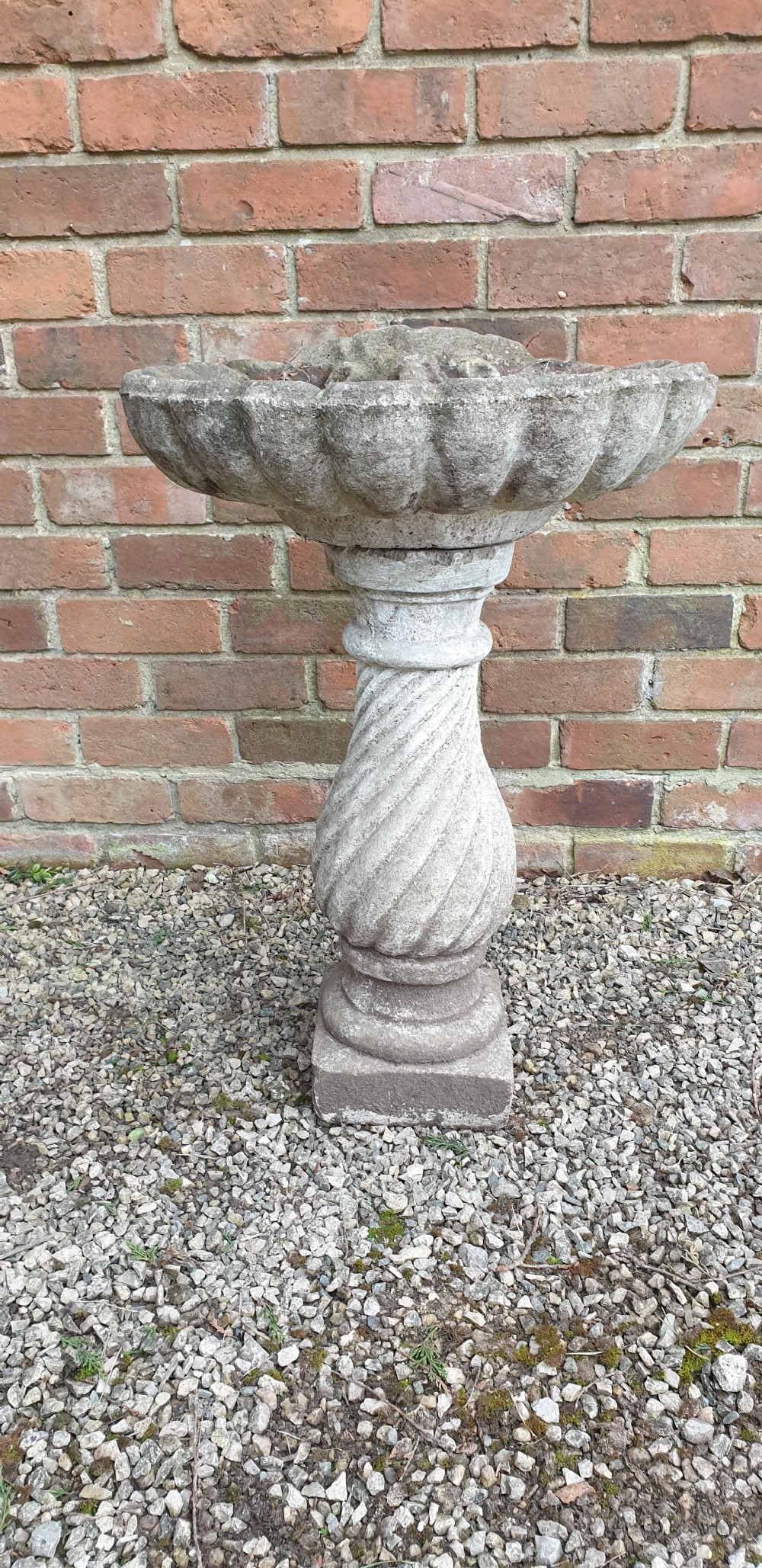 A weathered grey stone bird bath featuring a scalloped shell-shaped top basin set upon a spiral twisted pedestal column and square base. View III