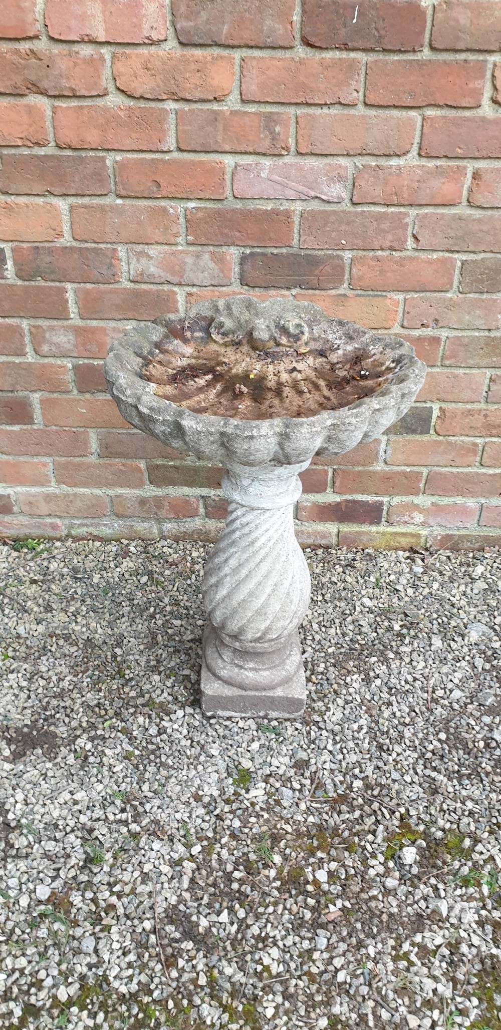 A weathered grey stone bird bath featuring a scalloped shell-shaped top basin set upon a spiral twisted pedestal column and square base. View VI