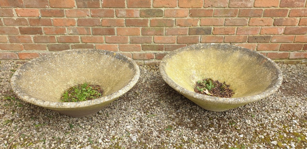 A pair of large shallow conical weathered stone pancheon bowls with visible moss patina resting on gravel. View II
