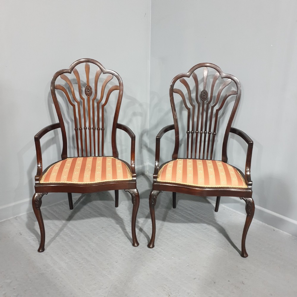 A pair of carved mahogany elbow chairs featuring openwork fan backs, swept armrests, terracotta striped upholstered seats, and cabriole front legs.