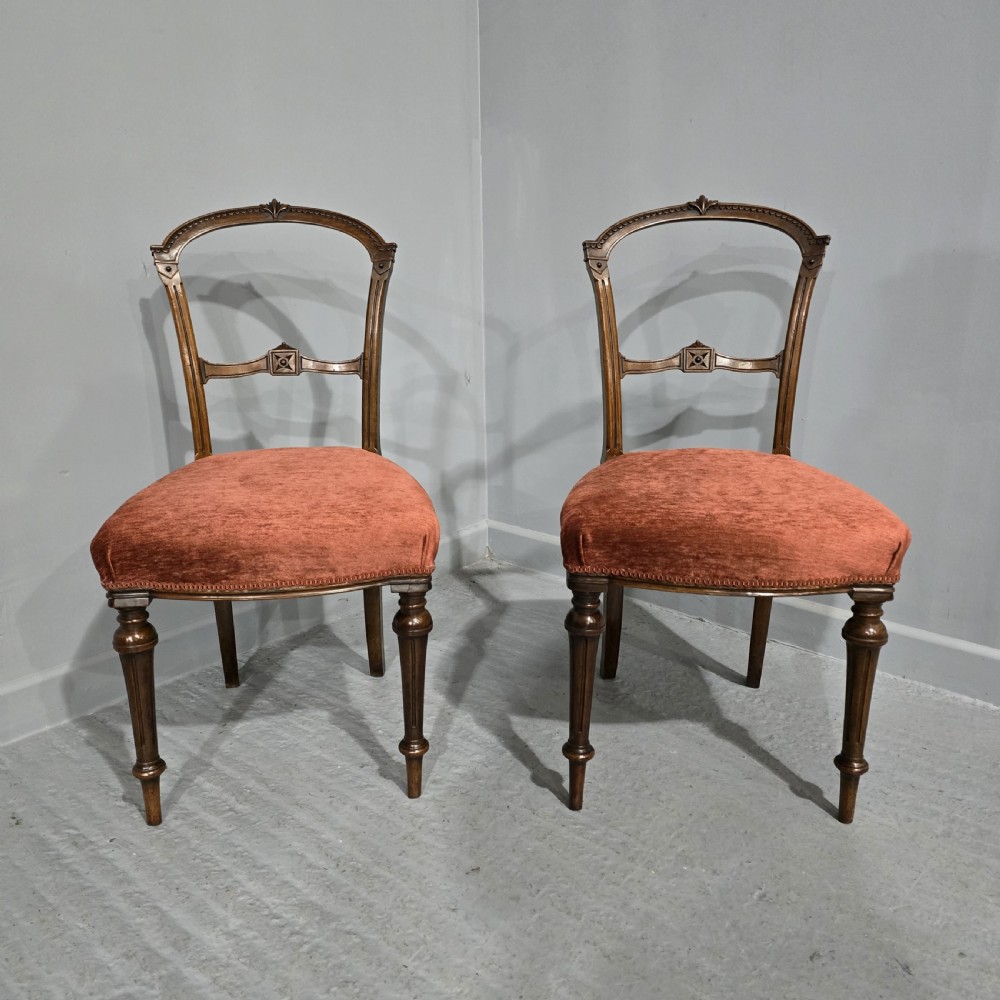 A pair of Victorian mahogany side chairs with openwork carved backs, turned front legs, and terracotta velvet seats.