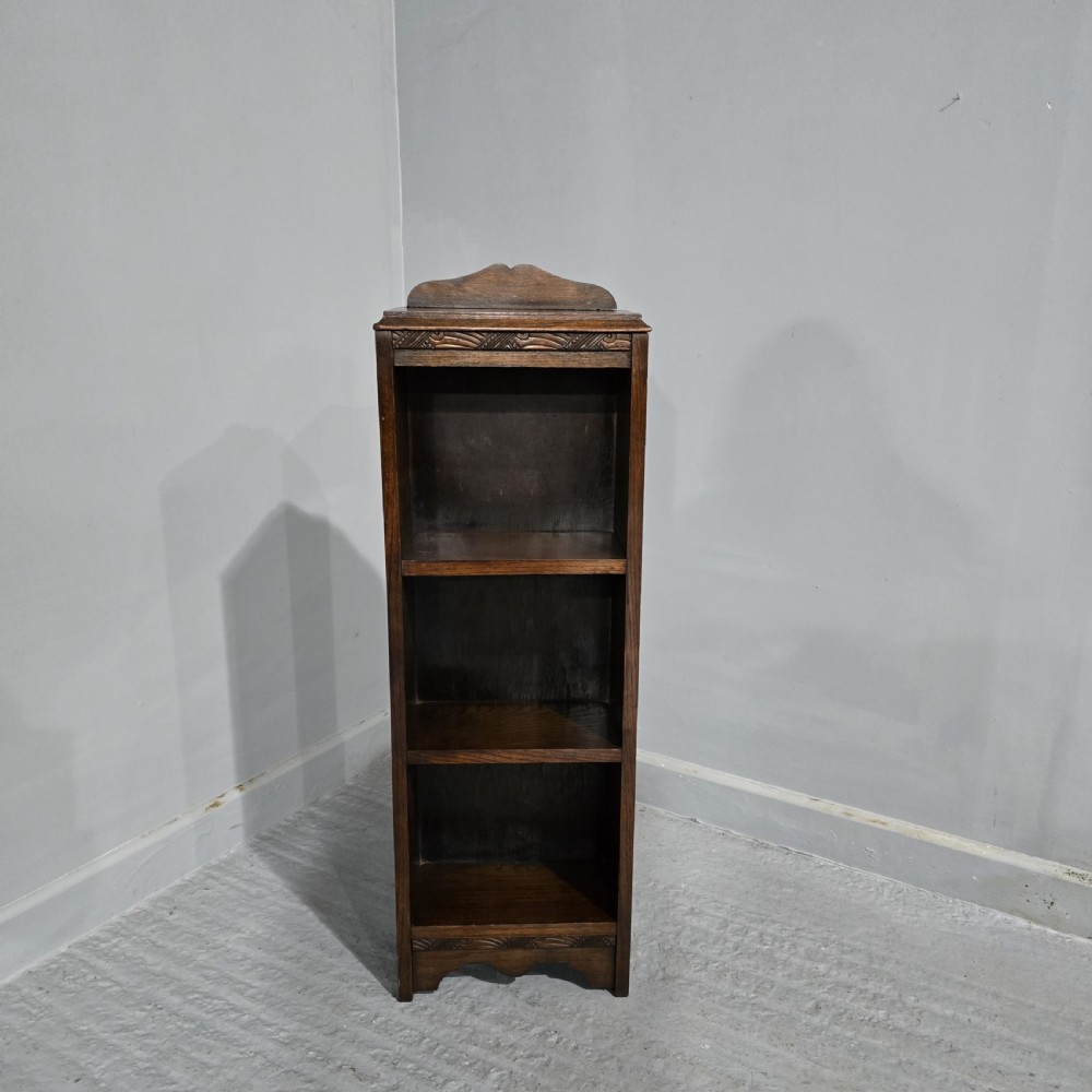 A narrow dark oak open bookcase featuring three fixed shelves, a crest gallery top, and a carved decorative frieze. View II