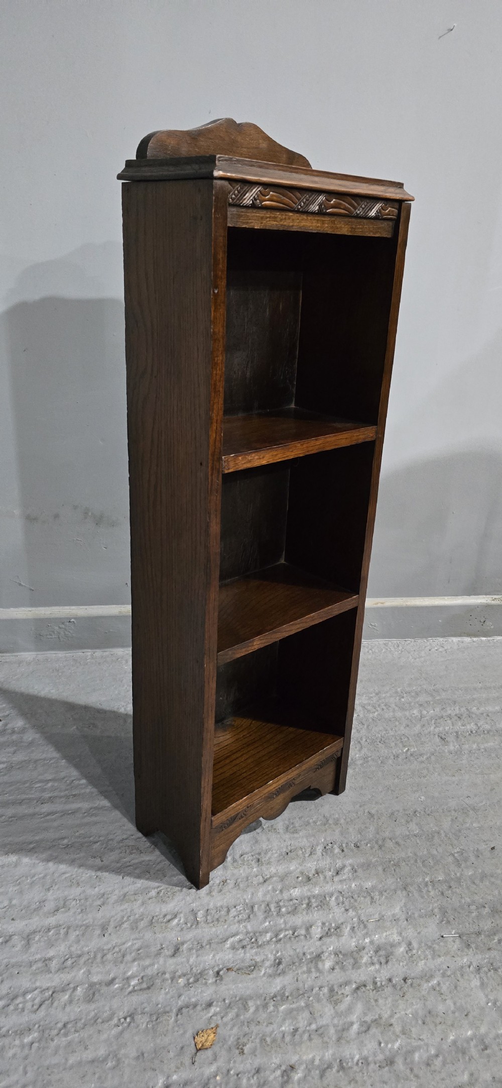 A narrow dark oak open bookcase featuring three fixed shelves, a crest gallery top, and a carved decorative frieze. View III