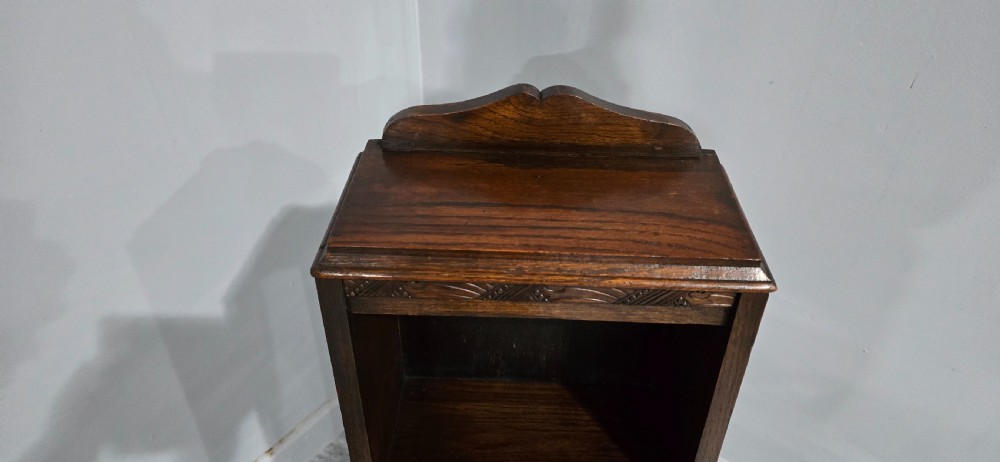 A narrow dark oak open bookcase featuring three fixed shelves, a crest gallery top, and a carved decorative frieze. View VI