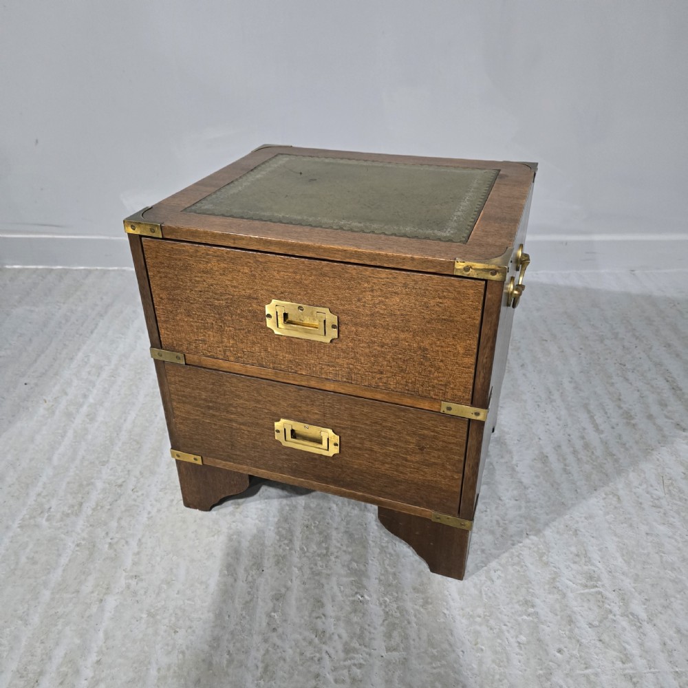 A small warm brown wooden campaign chest featuring two drawers, brass corner brackets, recessed brass handles, and a green leather inset top.