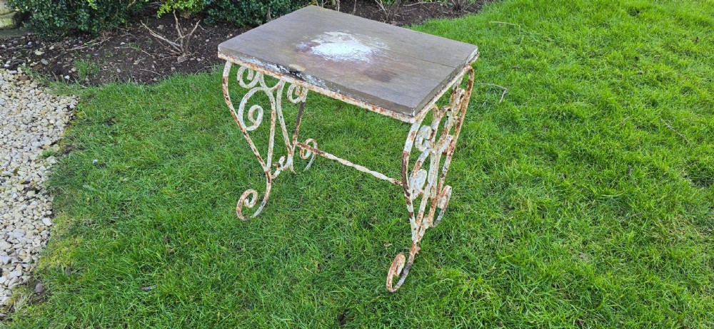 An antique garden side table featuring scrolled strapwork wrought iron legs in distressed off-white paint with a rectangular weathered wooden plank top. View II