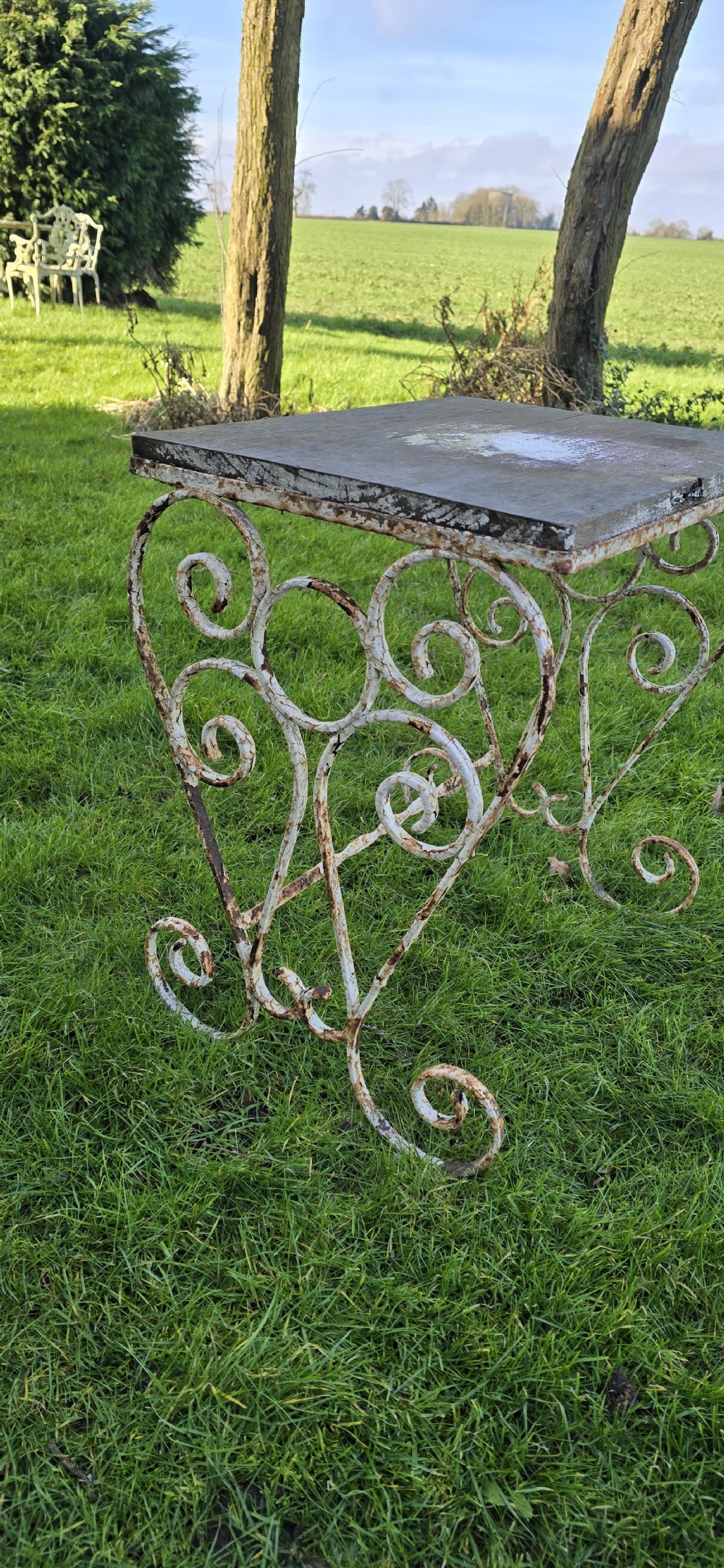 An antique garden side table featuring scrolled strapwork wrought iron legs in distressed off-white paint with a rectangular weathered wooden plank top. View III