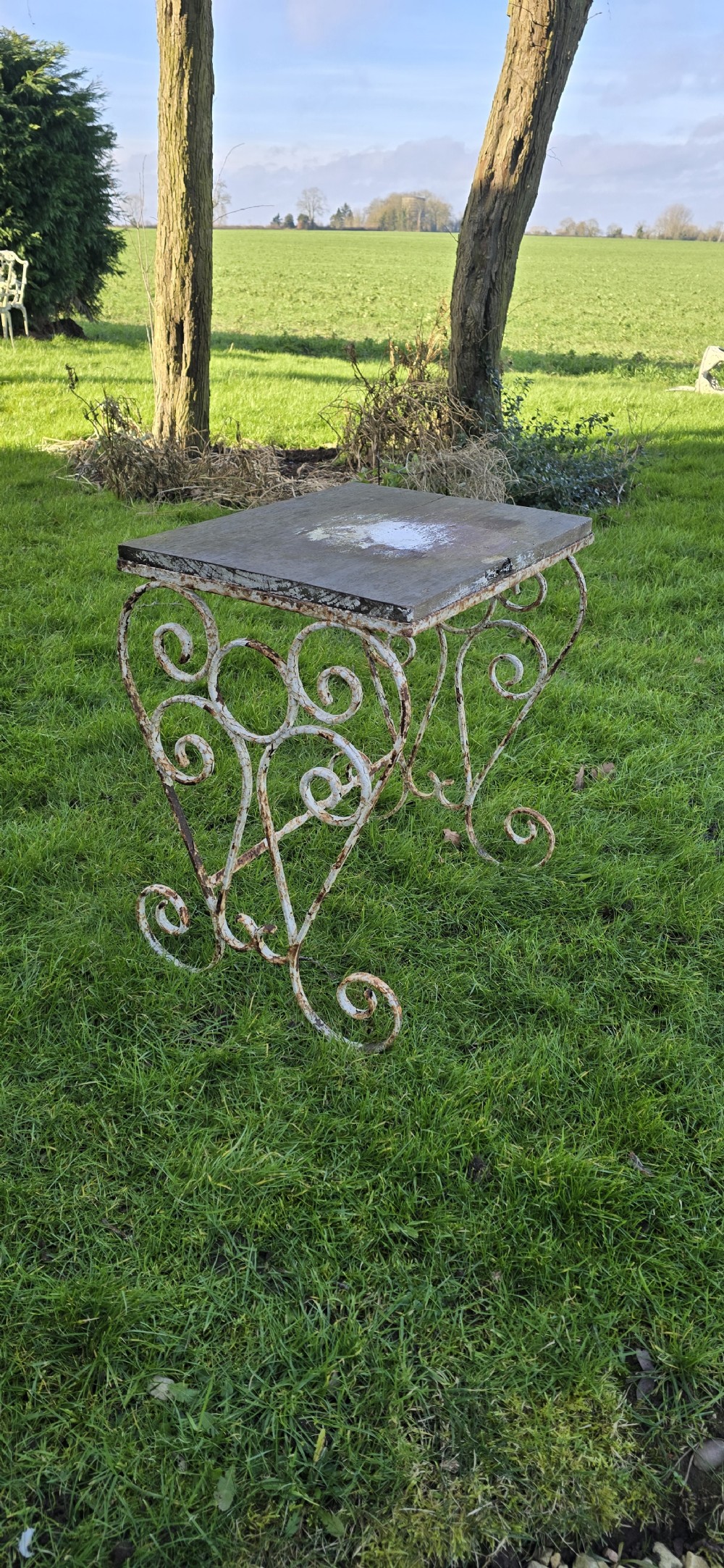An antique garden side table featuring scrolled strapwork wrought iron legs in distressed off-white paint with a rectangular weathered wooden plank top. View V