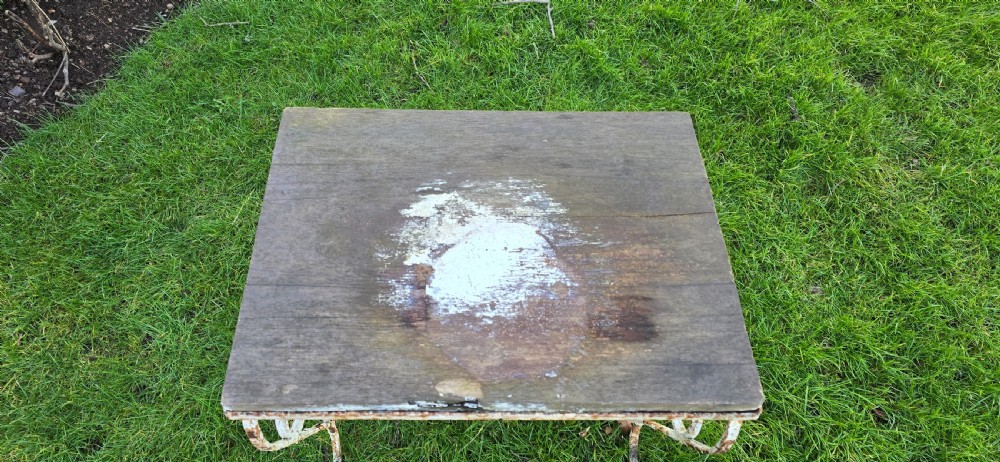 An antique garden side table featuring scrolled strapwork wrought iron legs in distressed off-white paint with a rectangular weathered wooden plank top. View VI