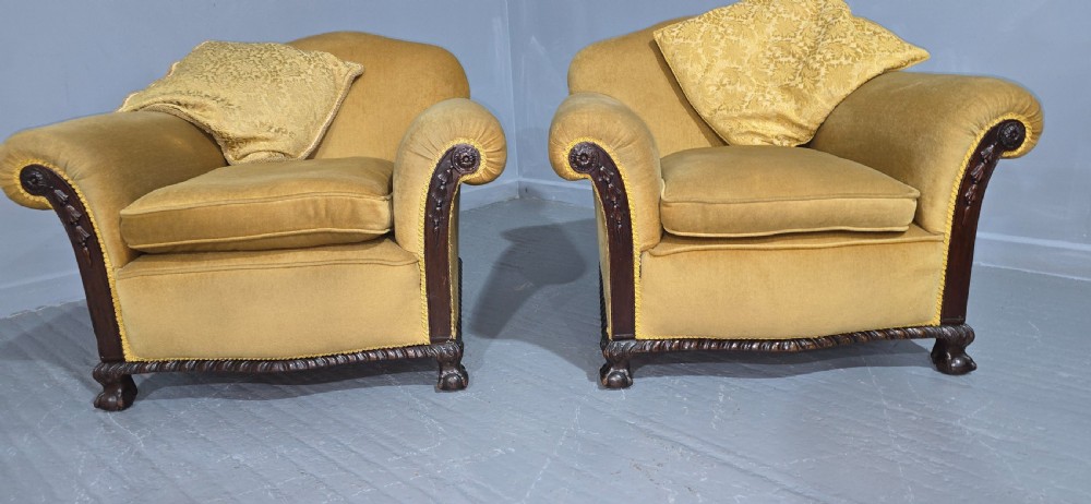 A pair of yellow velvet upholstered club chairs featuring carved dark timber trim along the front arms and base. View III