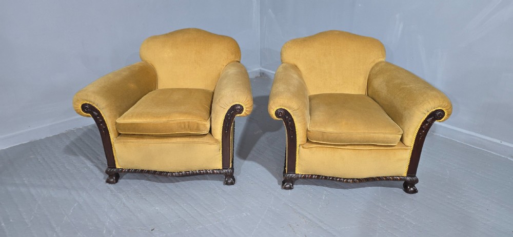 A pair of yellow velvet upholstered club chairs featuring carved dark timber trim along the front arms and base. View IV
