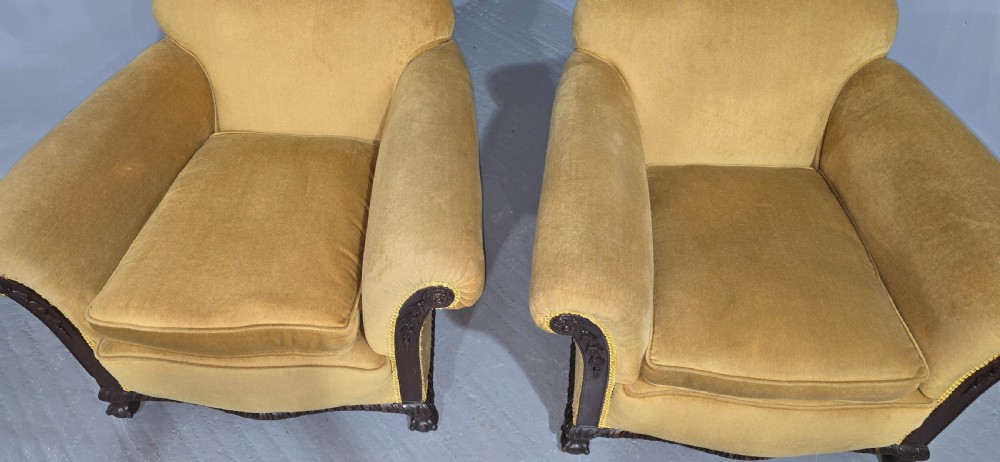 A pair of yellow velvet upholstered club chairs featuring carved dark timber trim along the front arms and base. View V