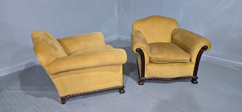 A pair of yellow velvet upholstered club chairs featuring carved dark timber trim along the front arms and base. View VII
