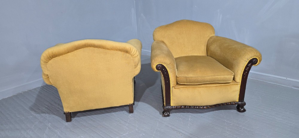 A pair of yellow velvet upholstered club chairs featuring carved dark timber trim along the front arms and base. View VIII
