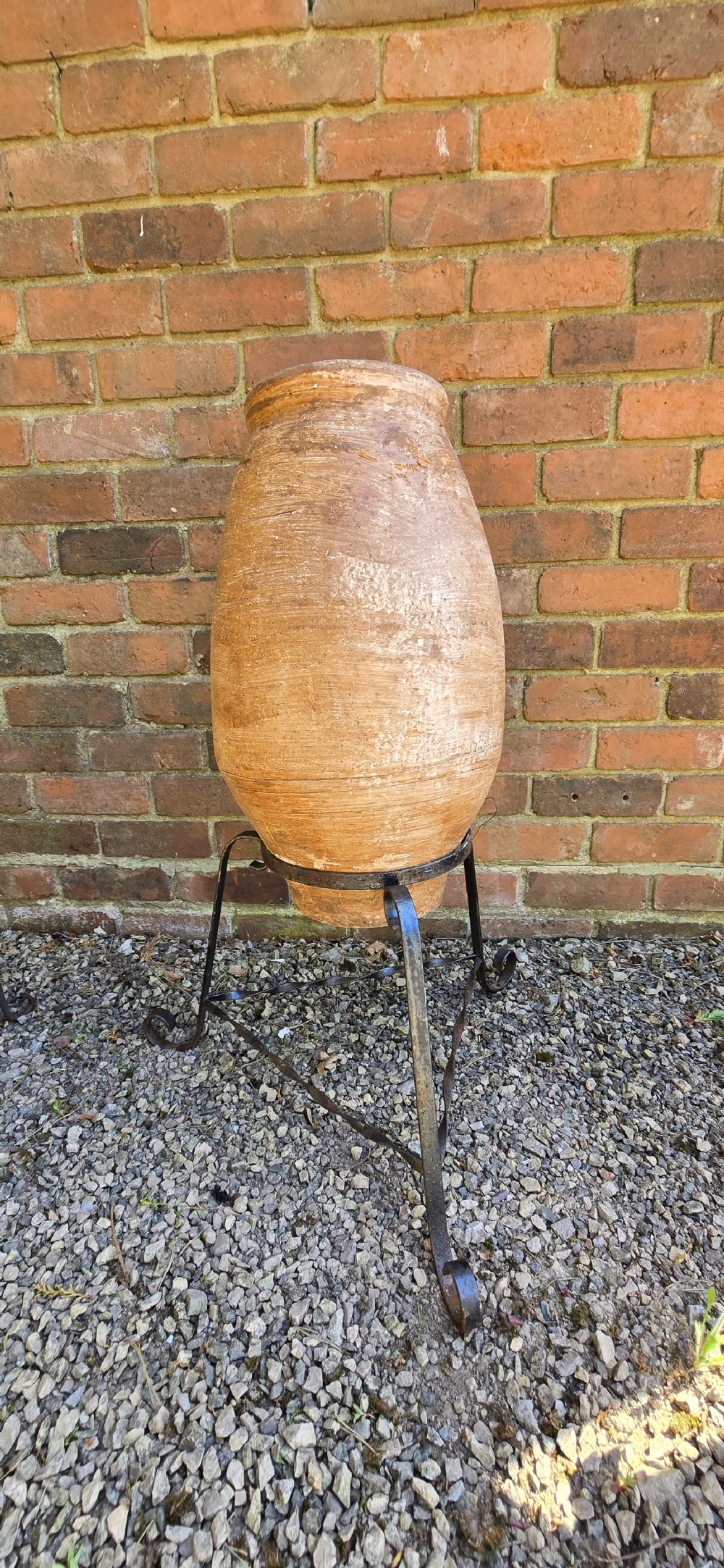 A pair of egg-shaped terracotta oil jars with weathered surfaces resting on black wrought iron tripod stands. View IV