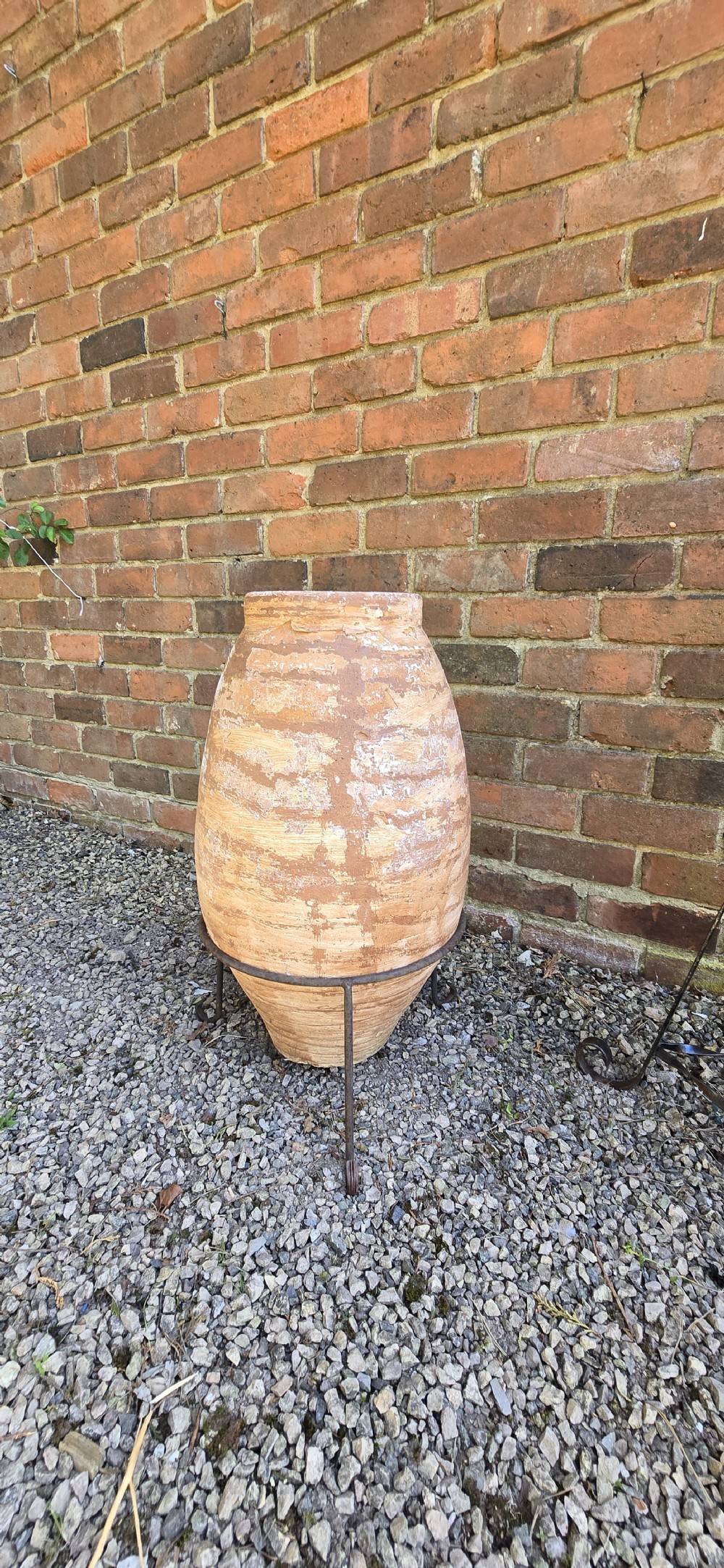 A pair of egg-shaped terracotta oil jars with weathered surfaces resting on black wrought iron tripod stands. View V