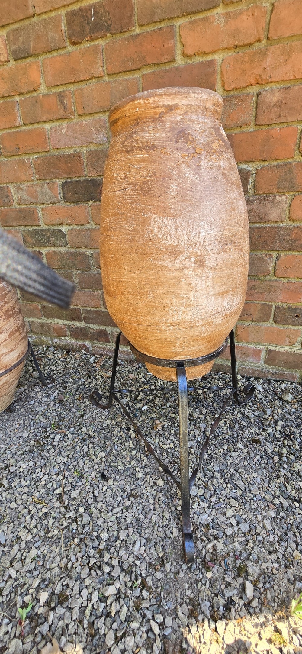 A pair of egg-shaped terracotta oil jars with weathered surfaces resting on black wrought iron tripod stands. View VI