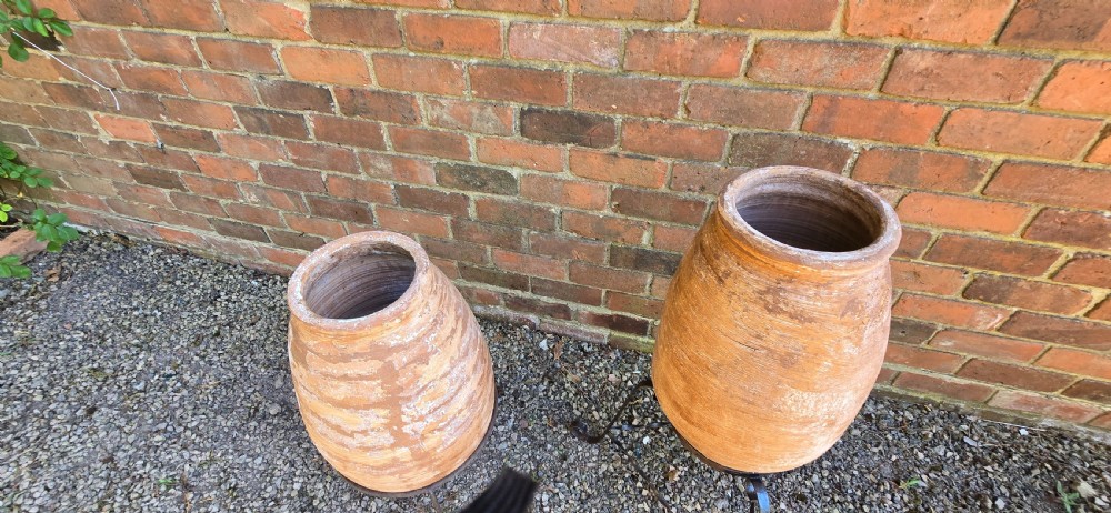 A pair of egg-shaped terracotta oil jars with weathered surfaces resting on black wrought iron tripod stands. View VII