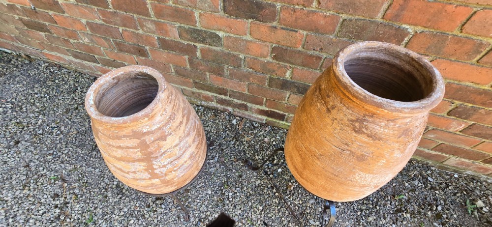 A pair of egg-shaped terracotta oil jars with weathered surfaces resting on black wrought iron tripod stands. View VIII