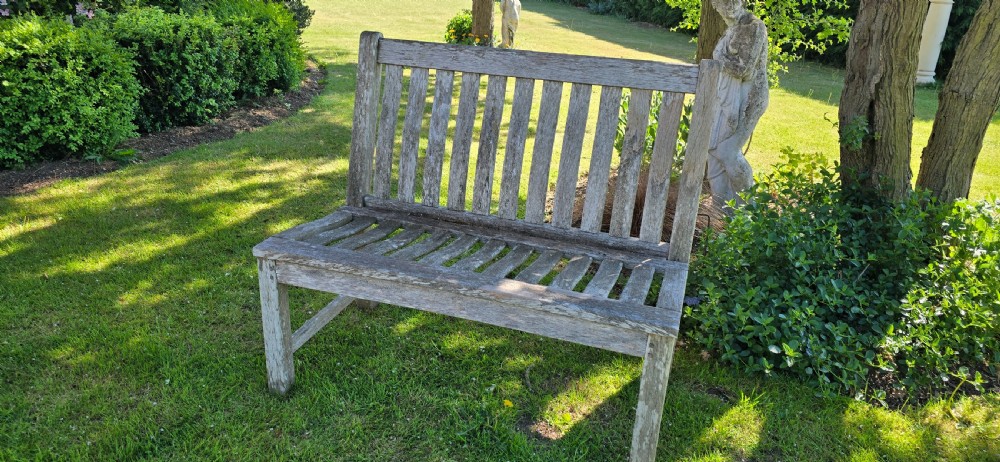 A slatted wooden garden bench with a naturally silvered weathered patina set outdoors on lawn grass. View III