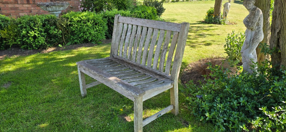 A slatted wooden garden bench with a naturally silvered weathered patina set outdoors on lawn grass. View V