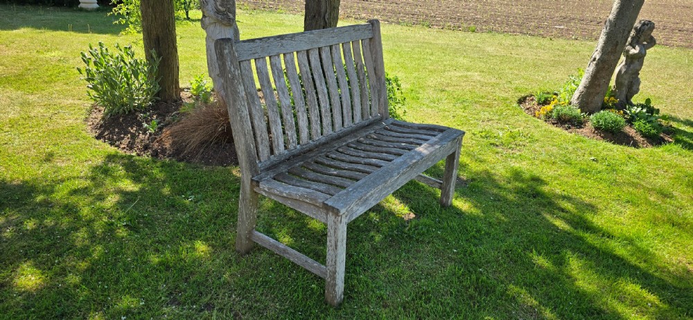 A slatted wooden garden bench with a naturally silvered weathered patina set outdoors on lawn grass. View VI