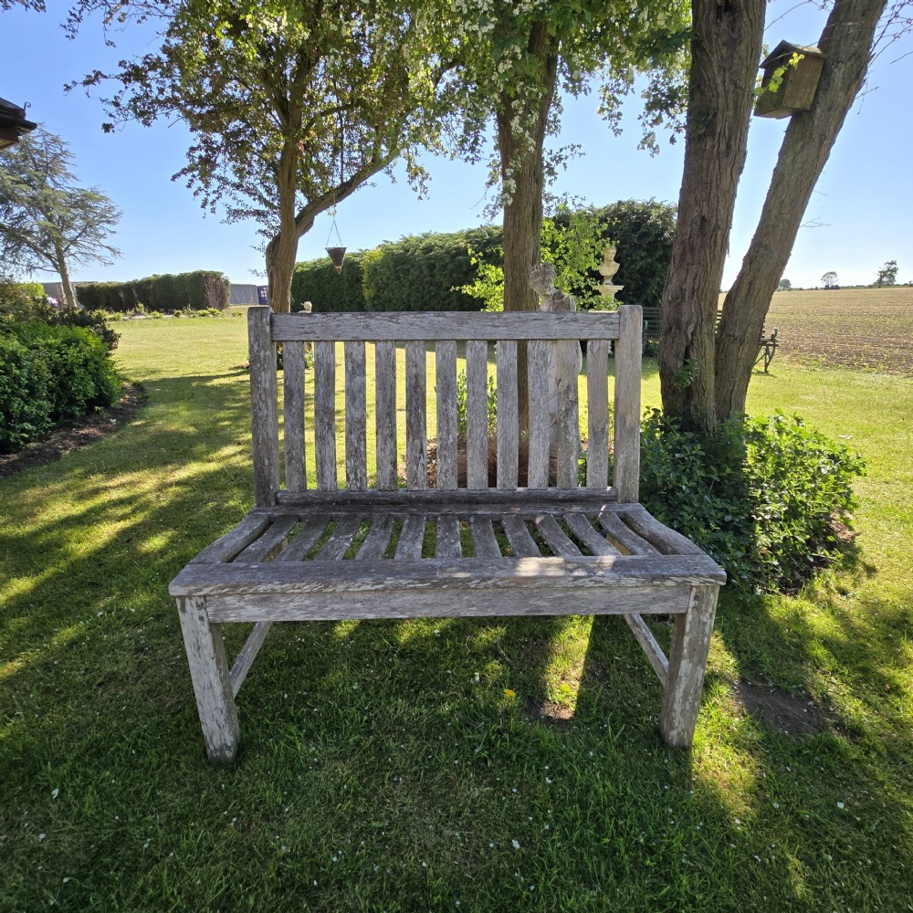 A slatted wooden garden bench with a naturally silvered weathered patina set outdoors on lawn grass.