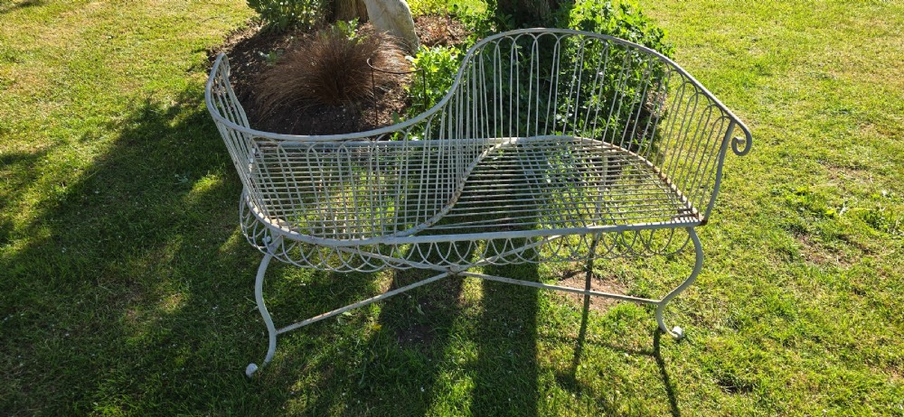A weathered off-white wrought iron garden love seat with an S-shaped double seat and vertical wirework backrest. View II
