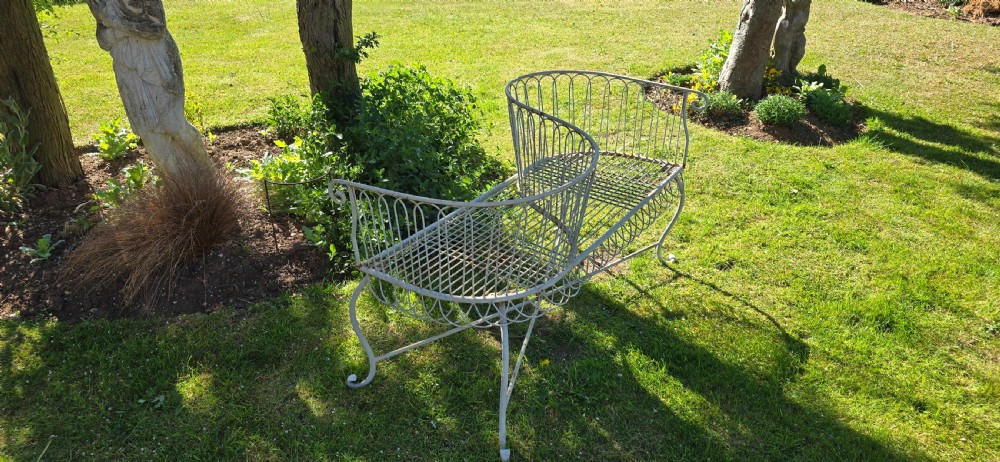 A weathered off-white wrought iron garden love seat with an S-shaped double seat and vertical wirework backrest. View III