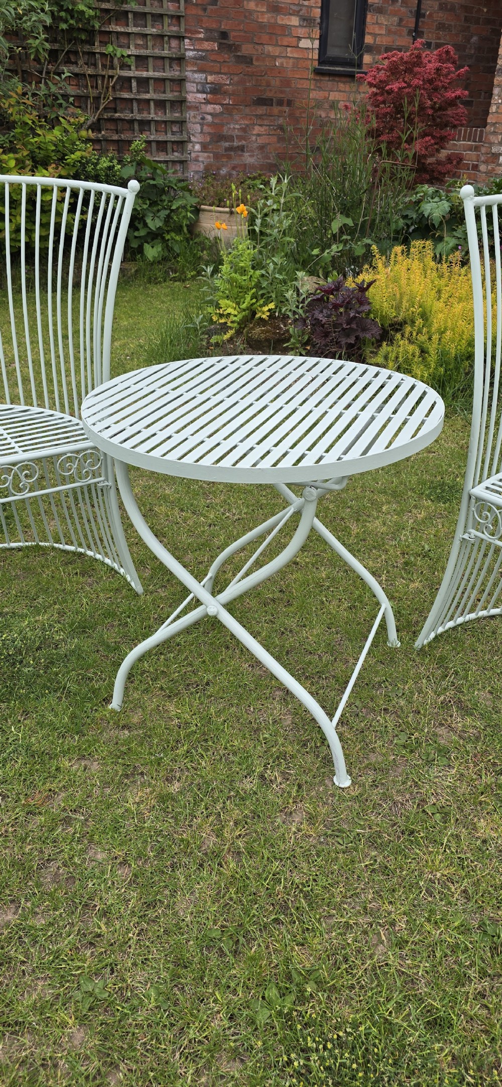 A three-piece pale green painted iron patio set featuring two high fan-back slatted armchairs and a small round folding bistro table. View II