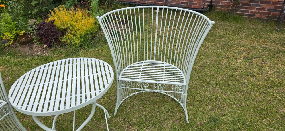 A three-piece pale green painted iron patio set featuring two high fan-back slatted armchairs and a small round folding bistro table. View IV