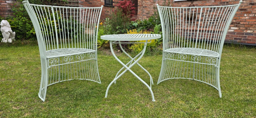 A three-piece pale green painted iron patio set featuring two high fan-back slatted armchairs and a small round folding bistro table. View V