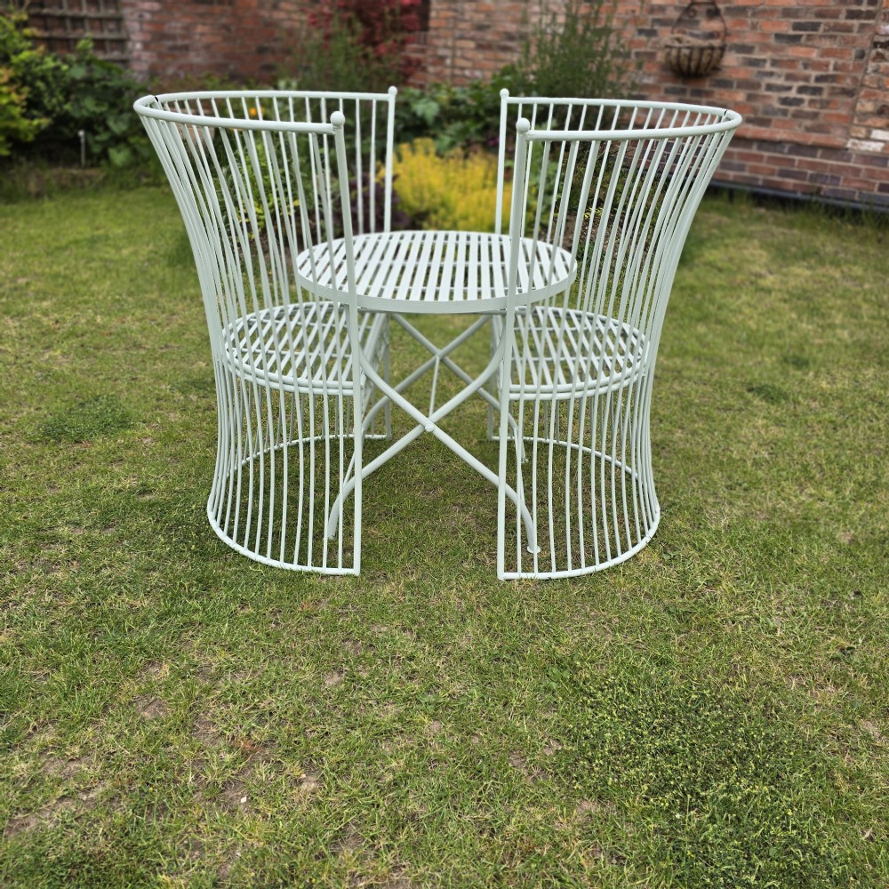 A three-piece pale green painted iron patio set featuring two high fan-back slatted armchairs and a small round folding bistro table. View VII