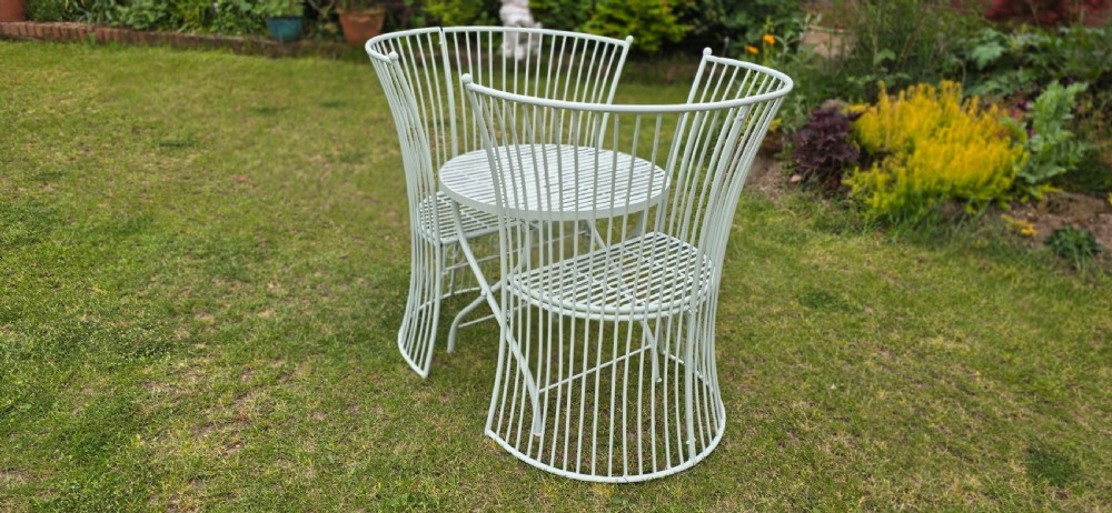A three-piece pale green painted iron patio set featuring two high fan-back slatted armchairs and a small round folding bistro table. View IX