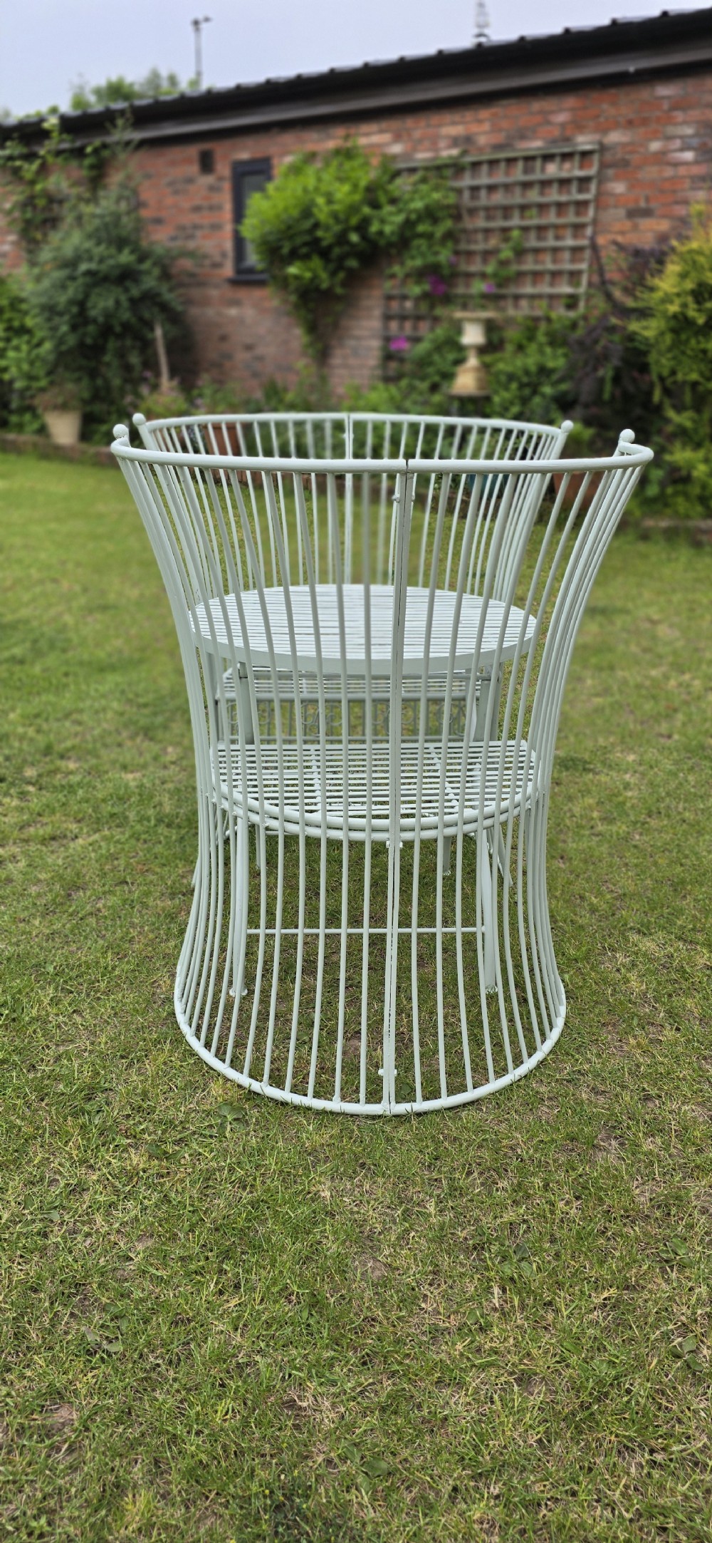 A three-piece pale green painted iron patio set featuring two high fan-back slatted armchairs and a small round folding bistro table. View X