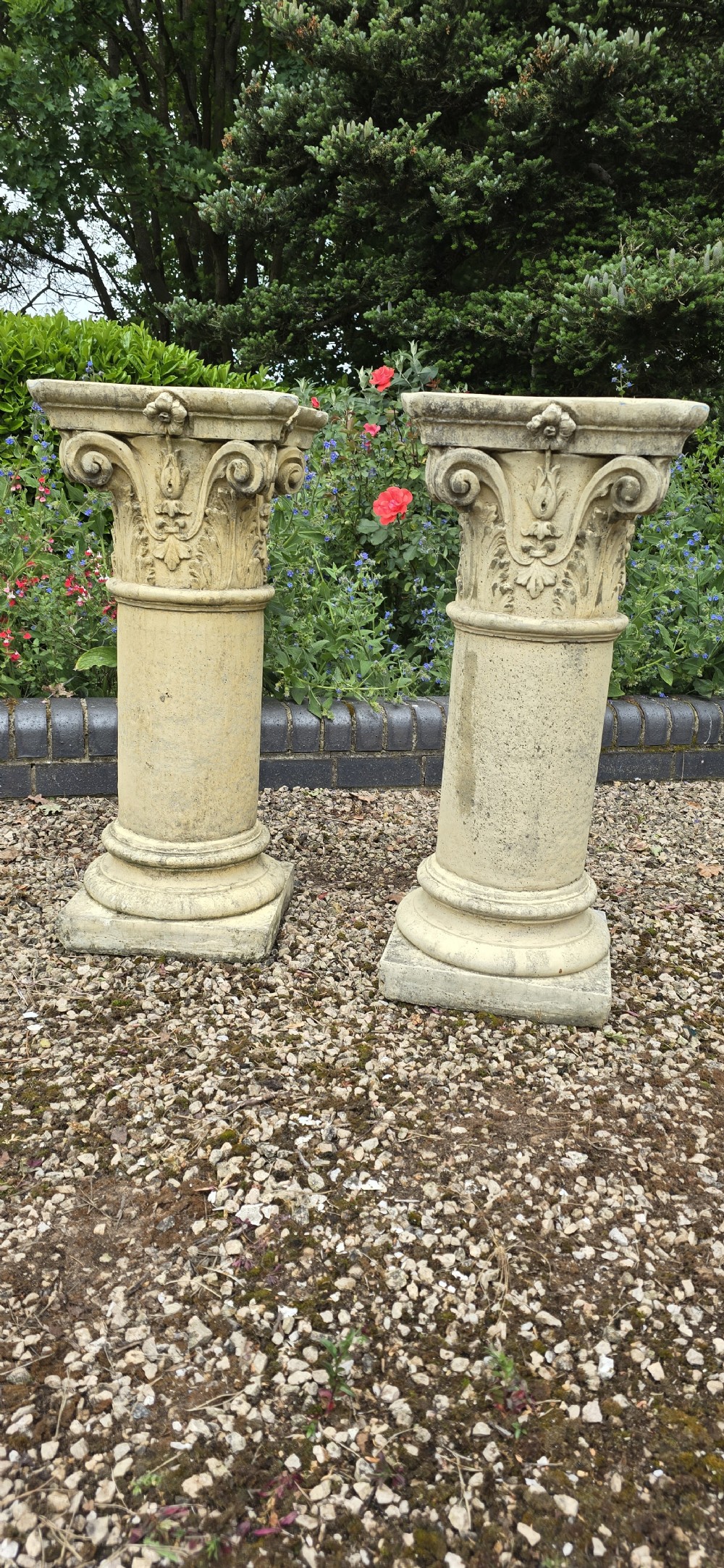 A pair of weathered buff cast stone Corinthian columns featuring acanthus leaf capitals and square bases. View II